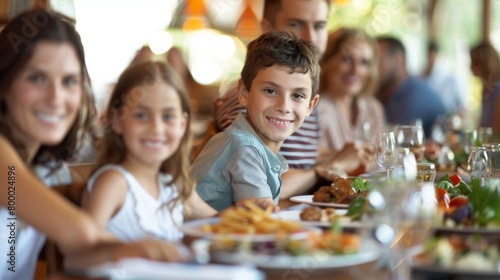 A joyful family gathering around a table filled with food and drinks with a young boy smiling at the camera.