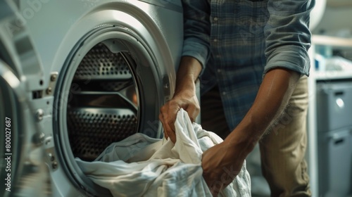 Man in blue shirt and khaki pants pulling white towel from front-loading washing machine. photo