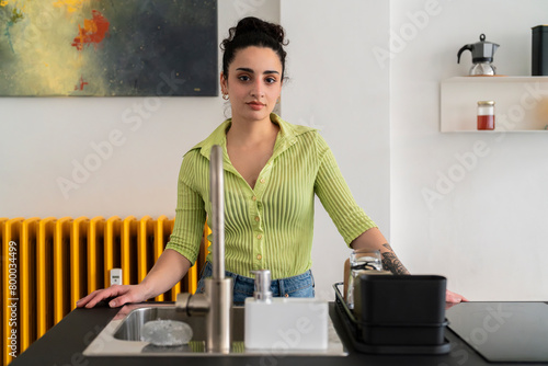 A confident woman stands by the sink in a modern kitchen with striking abstract art and vibrant yellow accents, blending style with domestic life photo