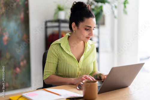 A focused South American woman in a lime-green shirt types attentively on her laptop, a glimpse into daily professional life photo