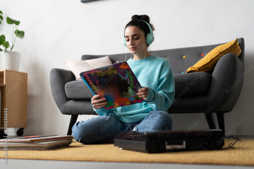 A young woman in a blue sweater examines a vinyl record, engaged in her passion for music, with a turntable and headphones nearby A young woman in a blue sweater examines a vinyl record, engaged in her passion for music, with a turntable and headphones nearby