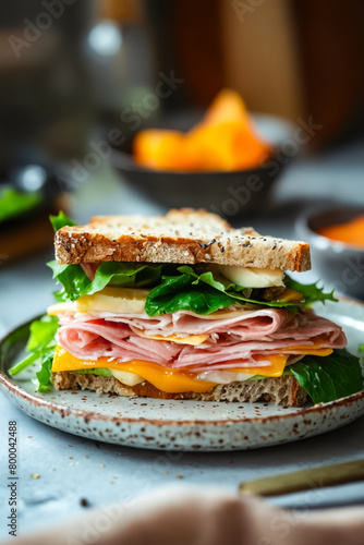 A sandwich with ham, cheese, and lettuce on a white plate. The sandwich is cut in half and placed on a table