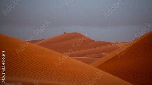 Solitary figure standing on orange sand dunes under a vast sky