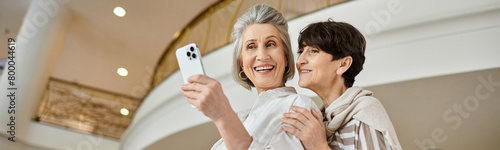 Senior lesbian couple joyfully taking a picture with her cell phone.