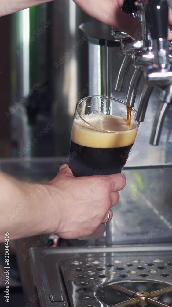 Barman pours dark beer into a glass from the beer tap in the pub. Bartender pouring perfect beer for client. Vertical video. Barman pours dark beer into a glass from the beer tap in the pub. Bartender pouring perfect beer for client. Vertical video.