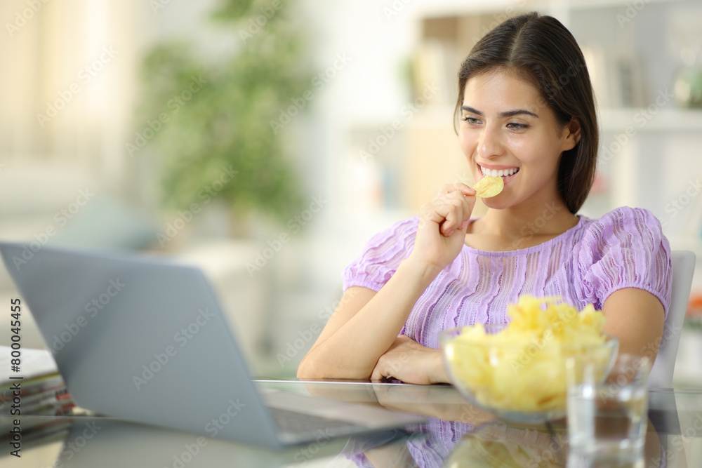 Happy woman eating potato chips watching media Happy woman eating potato chips watching media