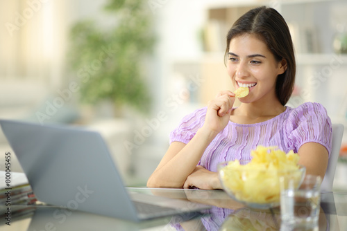 Happy woman eating potato chips watching media