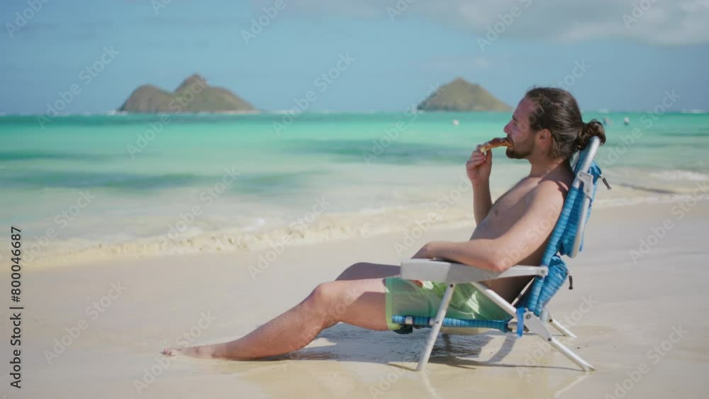 A man lounges in a beach chair, savoring a slice of pizza while basking in the warm tropical sun, with the serene turquoise sea creating a picture-perfect holiday scene. Slow motion. A man lounges in a beach chair, savoring a slice of pizza while basking in the warm tropical sun, with the serene turquoise sea creating a picture-perfect holiday scene. Slow motion.