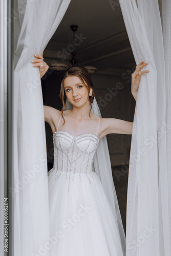 A woman in a white wedding dress is standing in front of a curtain. She is smiling and looking at the camera © Vasil