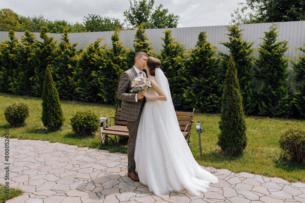 A bride and groom are standing in front of a bench, with the bride holding a bouquet A bride and groom are standing in front of a bench, with the bride holding a bouquet