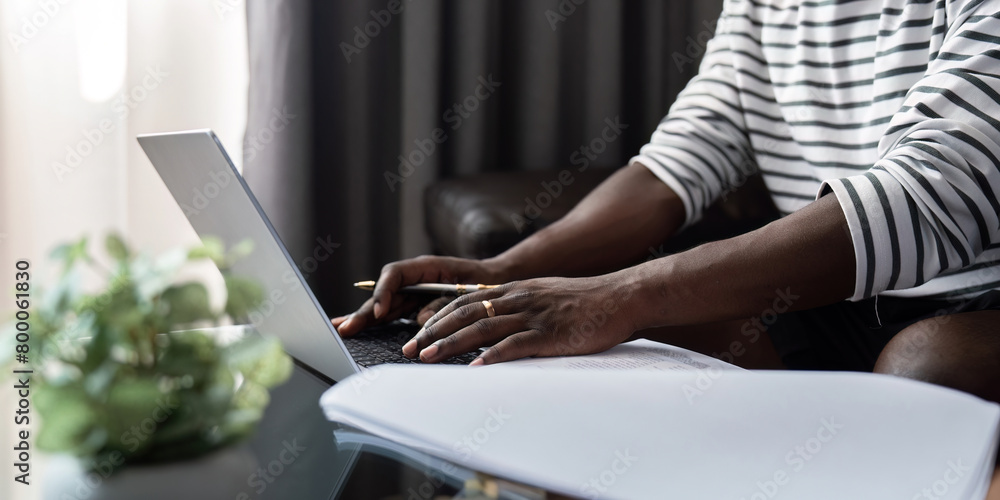African American man working with laptop computer video calling and conference, remote work while sitting at sofa in living room. Black guy do freelance work at home office African American man working with laptop computer video calling and conference, remote work while sitting at sofa in living room. Black guy do freelance work at home office