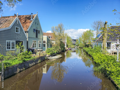 A dutch canal with wooden houses a lush, green countryside with vibrant foliage and rolling hills under a clear blue sky