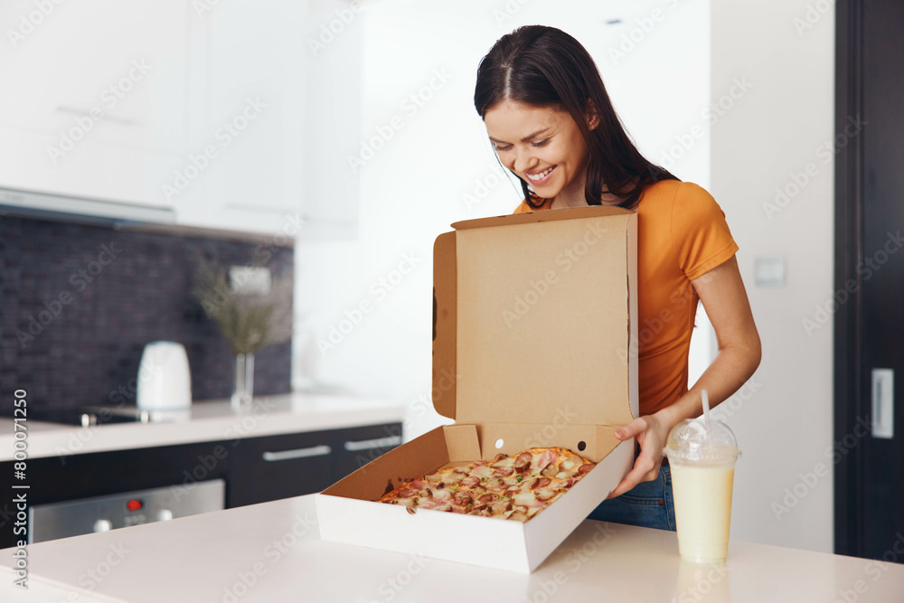 Young woman holding a box of pizza in kitchen setting Young woman holding a box of pizza in kitchen setting