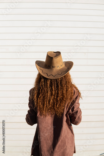 Curly haired woman wearing jacket and cowboy hat in front of white shutter