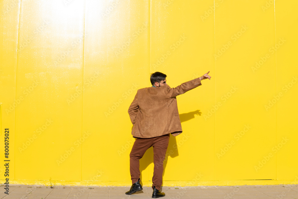 Man wearing brown jacket and dancing in front of yellow wall Man wearing brown jacket and dancing in front of yellow wall
