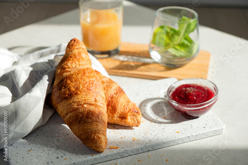 Fresh croissant for breakfast with jam on white board. Delicious celebratory breakfast in sunlight. Bakery or confectionery. Romantic morning meal.