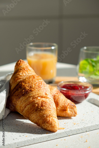 Fresh croissant for breakfast with jam on white board. Delicious celebratory breakfast in sunlight. Bakery or confectionery. Romantic morning meal.