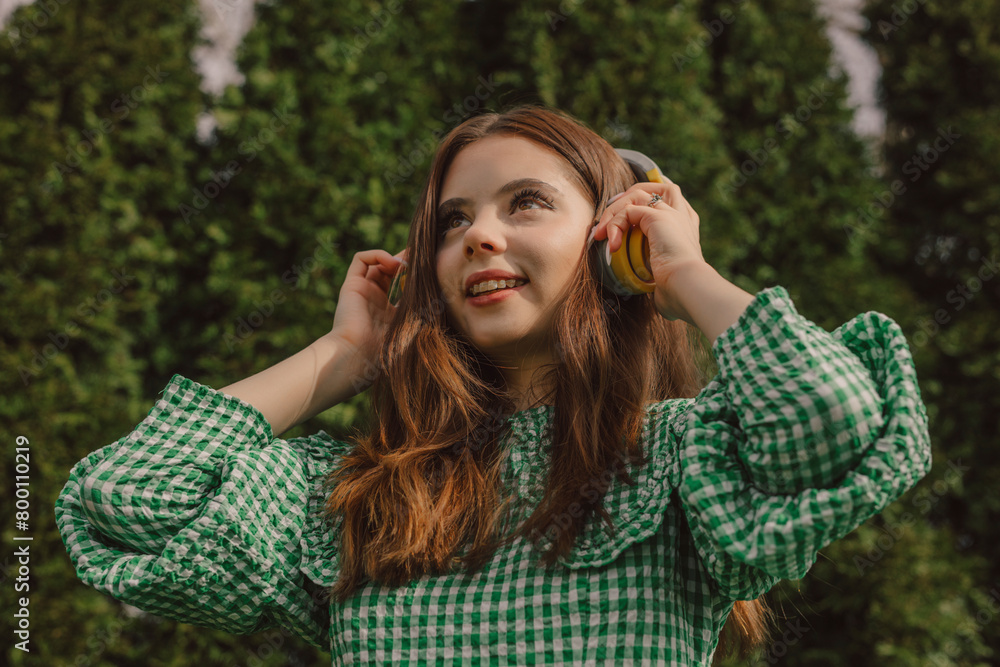 Smiling young woman wearing wireless headphones near trees Smiling young woman wearing wireless headphones near trees