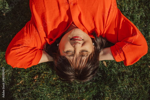 Smiling mature woman with hands behind head lying on grass in back yard photo