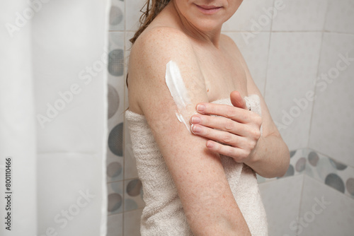 A slender girl with blond hair and delicate skin, in a white towel, smears her hand with cream. Image about cosmetics, beauty and health for your creativity.