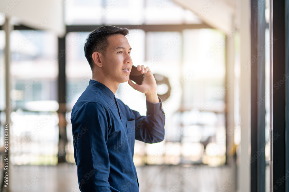 A focused businessman in a modern office setting engaged in a conversation on his mobile phone, embodying active business communication. A focused businessman in a modern office setting engaged in a conversation on his mobile phone, embodying active business communication.