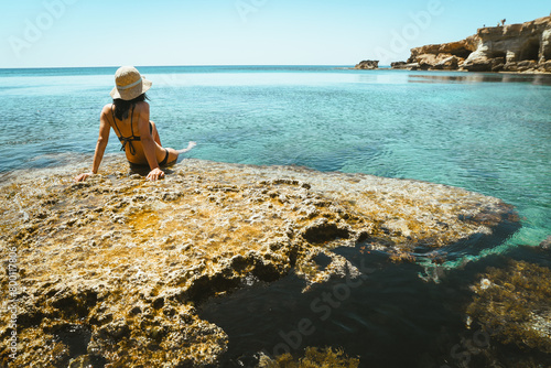 Beautiful caucasian woman sit on viewpoint rock enjoy crystal clear waters and mediterranean seascape panorama on summer holiday vacation. Happiness and travel explore concept photo