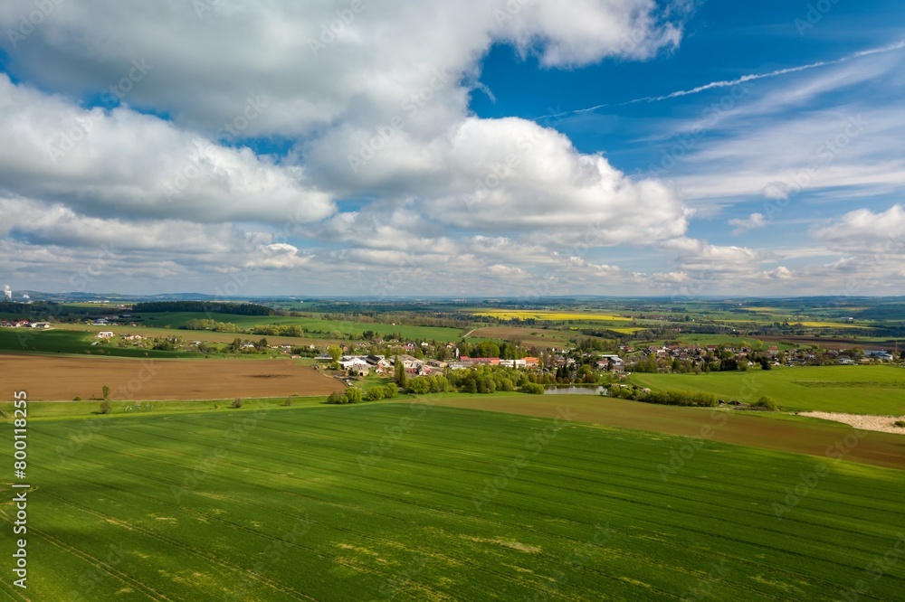 Drone flies over countryside with green wheat field. Hilly area with forest. Warm sunny spring day. Aerial view landscape. Beautiful rural landscape. Czech Republic