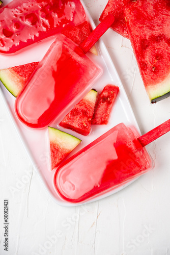 Overhead view of three watermelon lollies on white plate with watermelon pieces, white background, vertical, with copy space