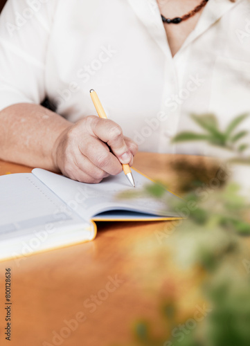 Elderly woman taking notes in a notebook. Close-up view of a woman sitting at a desk taking notes in a notebook while studying.