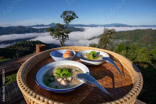 selective focus breakfast on a homestay on a mountain top, background view of misty mountains, clear sky Breakfast: porridge in a cup and boiled eggs on a wooden tray © Core