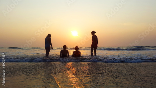 During the dawn on the beach four friends sitting near the sea and watching waves