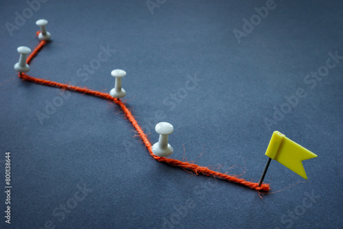Concept of achieving goals, planning and stages. Orange thread, pins and flag.