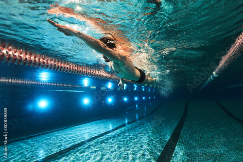sports advertising underwater photography of a swimmer in a pool swimming freestyle in a sports cap, swimming goggles and dark swimming trunks photo