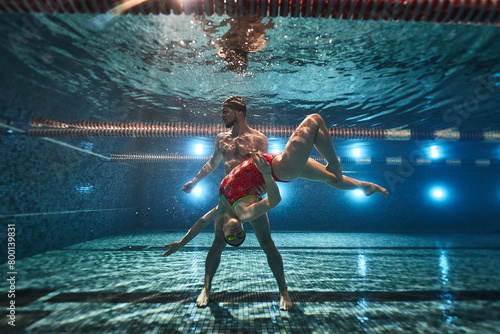 young athletes swimmers dive in the pool and under the water the guy holds the girl in his arms. synchronized swimming and posing. advertising underwater photography