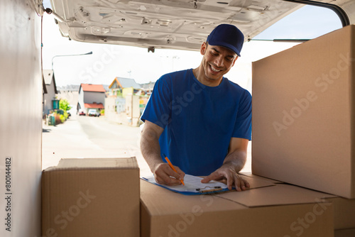 Foto Man courier writing data to clipboard while unloading boxes from van outdoors, g
