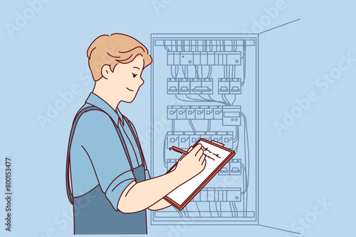Man inspector checks electrical equipment installed in metal power panel, makes notes in clipboard. Electrician guy stands near power panel, drawing up work plan for replacing wires. © drawlab19