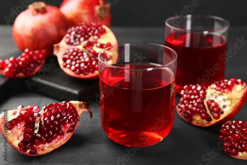 Tasty pomegranate juice in glasses and fresh fruits on black wooden table, closeup