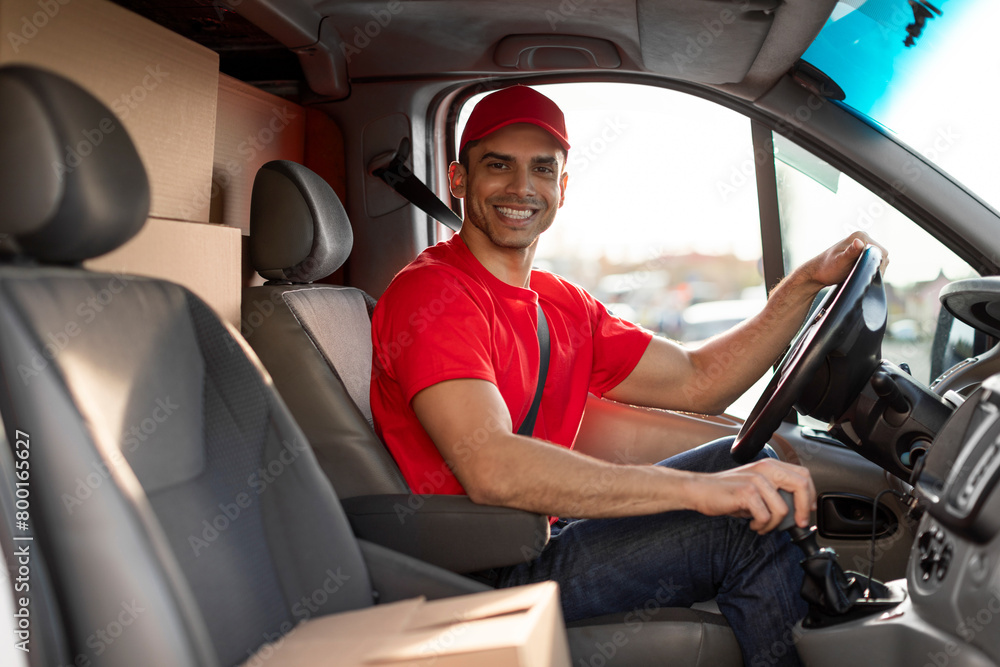 Happy young man courier driving delivery car and smiling at camera. Delivery and shipping concept