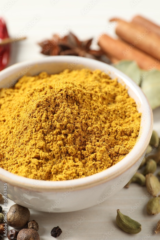 Curry powder in bowl and other spices on white wooden table, closeup