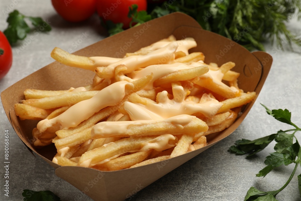 Tasty potato fries, cheese sauce in paper container and products on grey table, closeup Tasty potato fries, cheese sauce in paper container and products on grey table, closeup