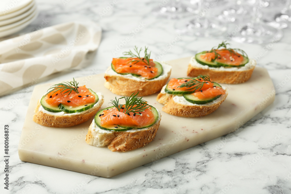 Tasty canapes with salmon, cucumber and cream cheese on white marble table