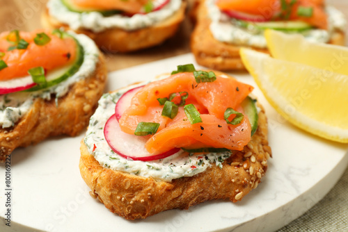 Tasty canapes with salmon, cucumber, radish and cream cheese on table, closeup