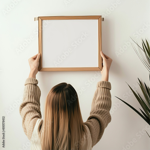 A girl hangs a white, empty frame on the wall
