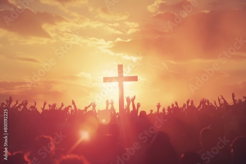 A crowd of various people are raising their two hands to the air to praise the Lord and gathered around a wooden cross settled at a mound among the cloudy sky. Religion and faith in God.
