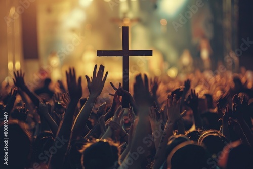 A crowd of various people are raising their two hands to the air to praise the Lord and  gathered around a wooden cross settled at a mound among the cloudy sky. Religion and faith in God. photo