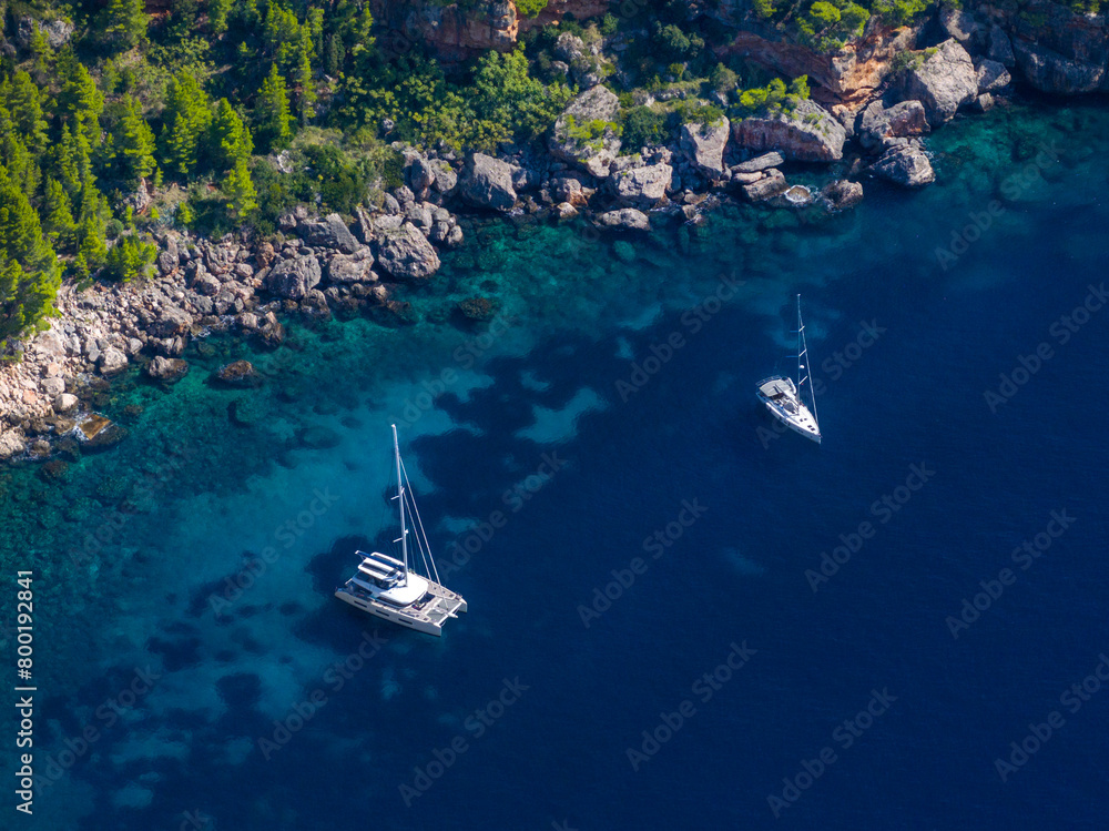AERIAL: Two luxury sailboats are anchored in the breathtaking turquoise sea. AERIAL: Two luxury sailboats are anchored in the breathtaking turquoise sea.