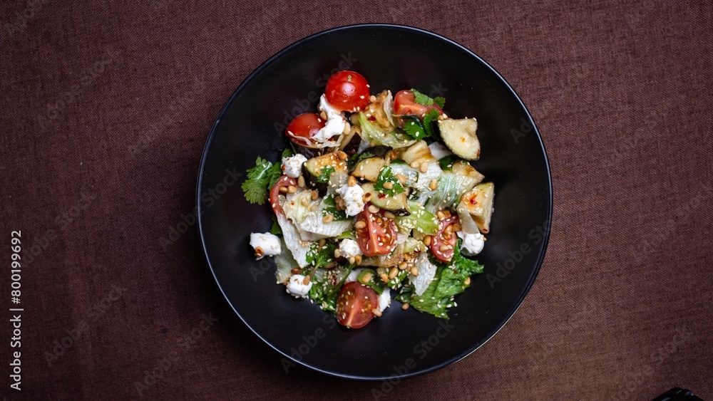 Black bowl of fresh salad with feta cheese and tomatoes on brown table Black bowl of fresh salad with feta cheese and tomatoes on brown table