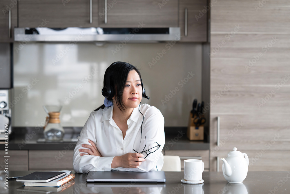 Young Asian professional woman working from home on her laptop while sipping a hot drink. Young Asian professional woman working from home on her laptop while sipping a hot drink.