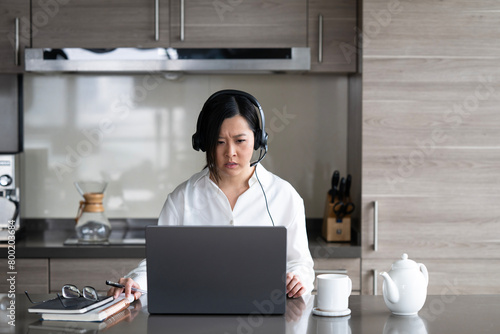 Young Asian professional woman working from home on her laptop while sipping a hot drink.