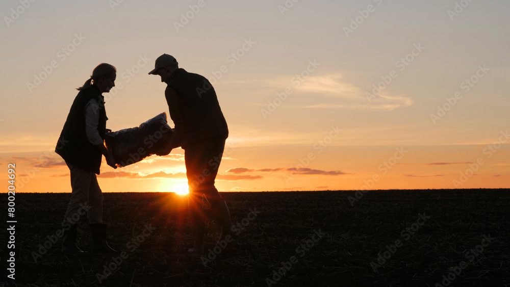 Two farmers with a bag of fertilizer. Standing in a field at sunset